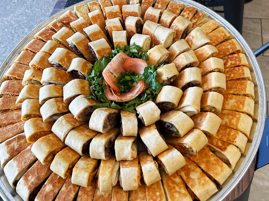 Family platter tray of saj shawarma wraps, sliced and arranged in rings around parsley and pickled turnip