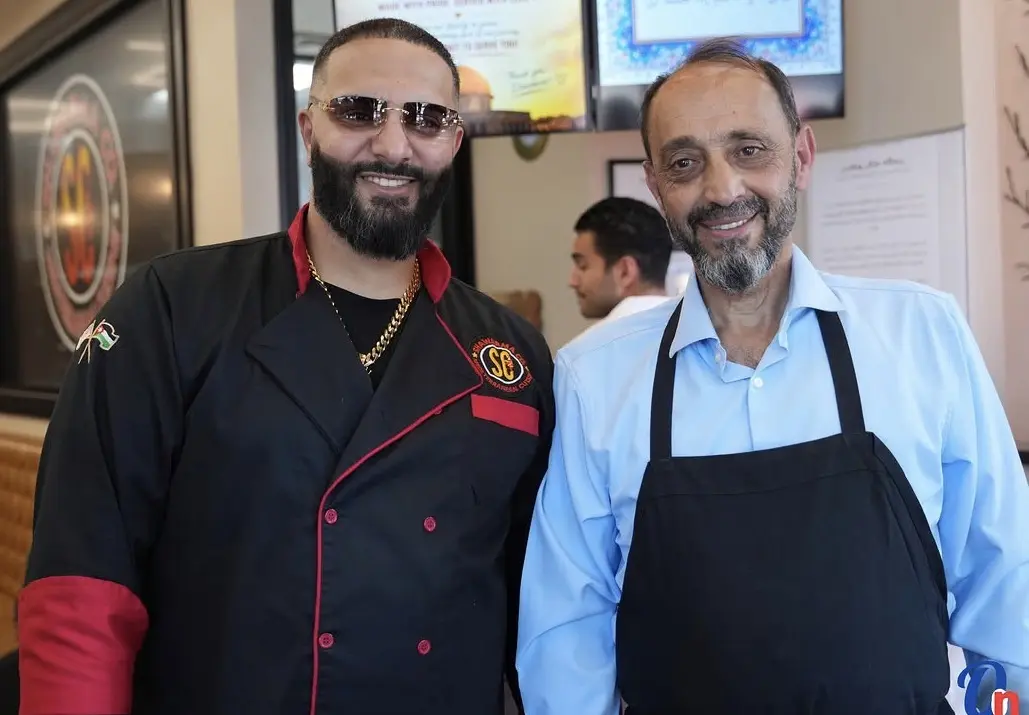 Shawarma Co founders Jafar, in a Shawarma Co chef coat, and his father Robeen, in an apron, standing inside the restaurant